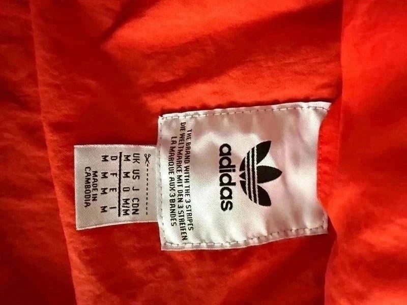 Metka wewnątrz pomarańczowej kurtki wiatrówki TrickandChic Adidas Originals z logo Trefoil i informacją o rozmiarze M