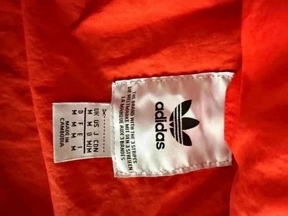 Metka wewnątrz pomarańczowej kurtki wiatrówki TrickandChic Adidas Originals z logo Trefoil i informacją o rozmiarze M