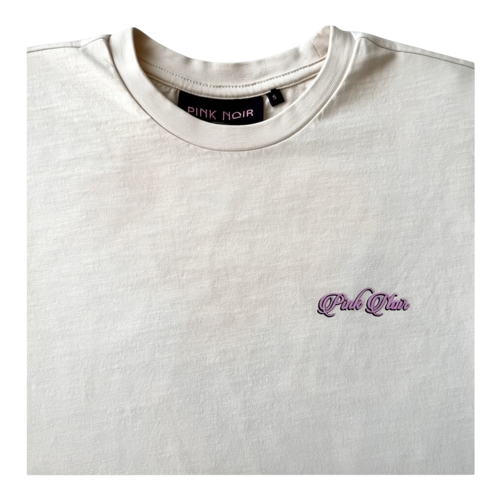 Zbliżenie kremowego T-shirtu Pink Noir: różowe logo na piersi, okrągły dekolt i metka w rozmiarze S