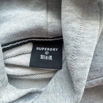 Metka marki Superdry wewnątrz szarej bluzy z kapturem TrickandChic z widocznym logo i japońskimi znakami